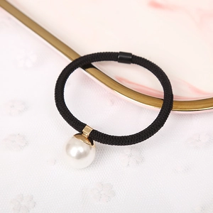 Close-up of black elastic hair tie with large white pearl on marble tray