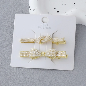 Detailed macro view of gold-tone knot and bow hair clips with white pearls on a card