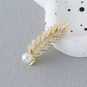 Détail d'une pince à cheveux feuille dorée avec pierres œil de chat, strass et perle