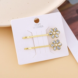 Detailed view of two gold hair clips with white marble floral patterns on white card