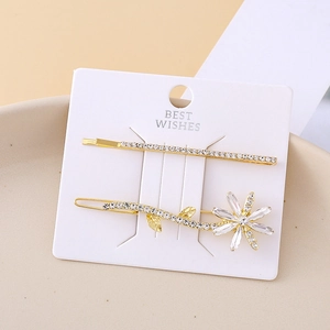 Set of two gold daisy hair clips with clear rhinestones on a white display card