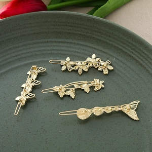 Detailed view of four golden alloy hair clips with flower and butterfly designs