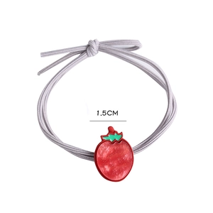 Gros plan d'un élastique à cheveux gris orné d'un pendentif fraise rouge détaillé de 1,5 cm