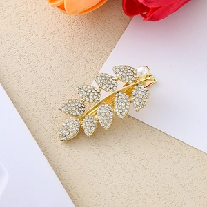 Barrette feuille dorée élégante avec strass en cristal et perle blanche sur fond beige