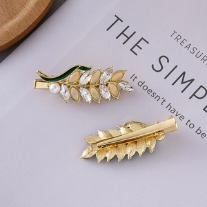 Close-up of wheat ear hair clip with green enamel, gold finish and pearl detail
