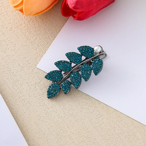 Détail macro d'une pince à cheveux feuille avec strass bleu paon et perle blanche