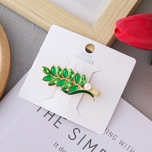 Elegant green leaf hair clip with golden metal base, crystals and pearl on a white card