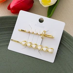 Set de barrettes dorées avec perles en cœur et nœud en strass sur plateau vert