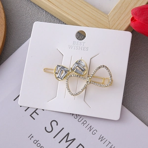 Golden double bow hair clip with crystals and rhinestones shown on a display card