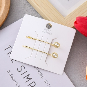 Close-up of two gold-plated hair clips with oval crystals on a white display card