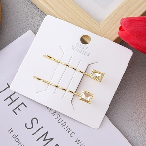 Detail view of two gold metal hairpins with square clear crystals on a white display card