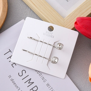 Close-up of silver alloy hair clips with square crystal stones on a white card display