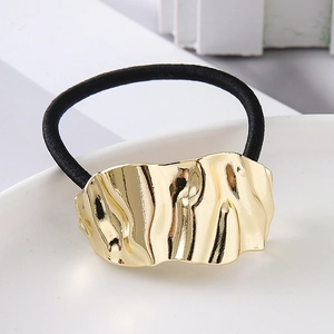 Close-up of golden wavy metal decorative plate on a premium black elastic hair tie