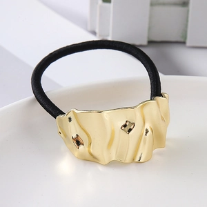Detailed close-up of golden irregular metallic curved accent on black elastic hair tie