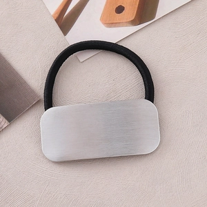 Minimalist silver brushed metal rectangle hair tie on a textured beige fabric background