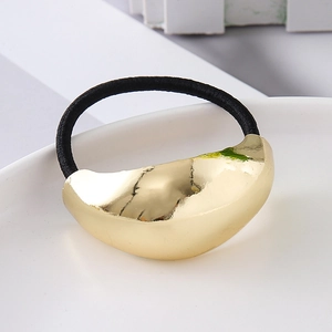 Macro shot of polished gold metallic curved hair tie with black elastic band on white plate