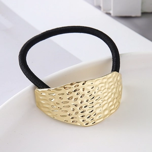 Detail of minimalist golden hammered metal plate on a black elastic hair tie