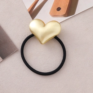 Close-up of golden matte heart charm with black elastic hair tie on pink background