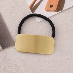 Macro detail of high-elastic black hair tie with premium brushed gold metal rectangle plate