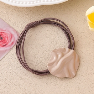 Brown multi-strand hair tie with beige irregular wave resin accent on warm background
