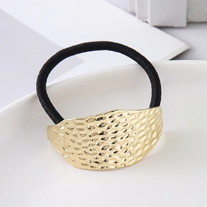 Detailed macro of gold hammered irregular metal charm on elastic black hair tie for women