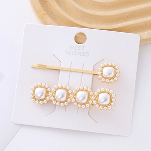 Détail de deux barrettes dorées avec perles carrées d'imitation sur carte de vente