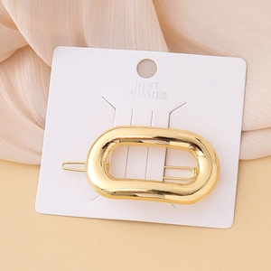 Detailed view of a polished hollow oval golden hair clip on a Best Wishes display card