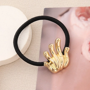 Élastique à cheveux minimaliste avec main de squelette dorée posée sur un plateau blanc