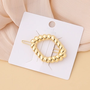 Close-up of golden oval hair clip with twisted texture on a white display card