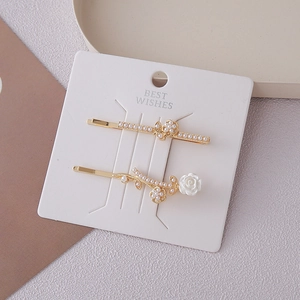Detail view of gold butterfly hair clips with pearls and rose flower on a card