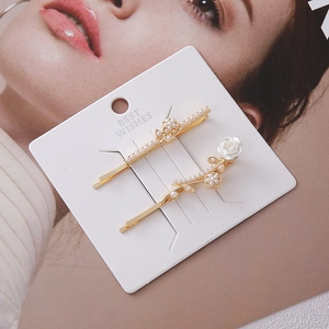 Detail of two gold hair clips featuring white resin rose and elegant faux pearls