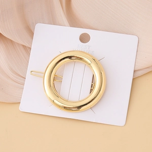 Detailed view of a circular gold metal hair clip displayed on a minimalist white card