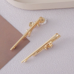 Detailed close-up of two golden metal hair pins with elegant white resin flower accents
