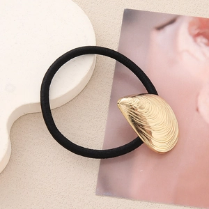 Détail d'une breloque coquillage dorée minimaliste sur un élastique à cheveux noir