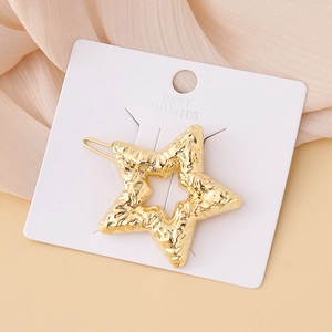Close-up of golden star-shaped hair clip with hammered texture on elegant fabric