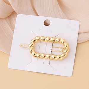Macro detail of elegant twisted gold metal hair clip on white presentation card