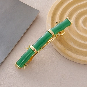 Eleganter jadefarbener Bambus-Haarclip mit goldenen Blattakzenten auf neutralem Grund