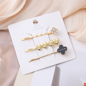 Three-piece gold hair clip set with rhinestone flower, heart design, and clover