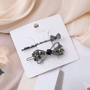 Detailed close-up of bow hair clips with dark grey and black rhinestones on silk