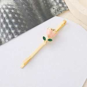 Detalle de una horquilla dorada elegante con rosa de esmalte rosa y pequeñas hojas verdes