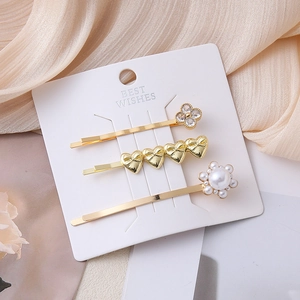 Three-piece gold hair clip set with clover, heart and pearl designs on a display card