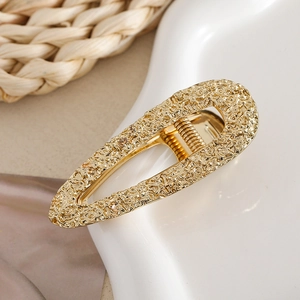 Close-up of golden teardrop hair clip with hammered lava texture on a ceramic tray