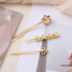 Detailed view of three gold hair clips with flower, heart, and clover motifs on silk fabric
