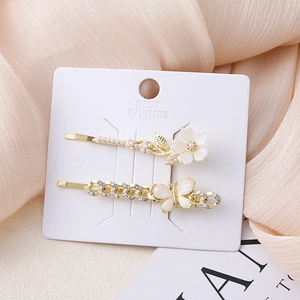 Detail van twee gouden haarspelden met witte bloemen, parels en een kristallen vlinder