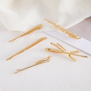 Détail de cinq barrettes à cheveux dorées minimalistes disposées sur un fond de tissu soyeux
