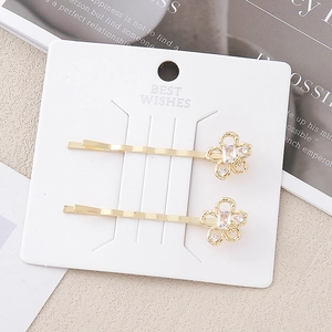 Détail de deux barrettes à fleurs dorées ornées de cristaux sur une carte décorative