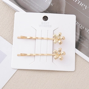 Détail de pinces à cheveux dorées avec fleurs et strass posées sur une carte cadeau