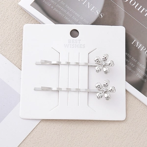 Détail de deux barrettes à fleurs argentées ornées de strass sur cartonnette
