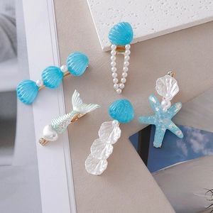 Detail of nautical hair clip set with blue seashells, starfish, and pearls on gold clips