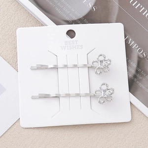Gros plan de barrettes fleurs argentées avec cristaux brillants sur une carte blanche